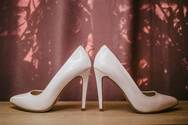 Anello diamante oro tra un paio di scarpe bianche con tacco alto. Dettagli matrimonio su sfondo rosso — Foto Stock