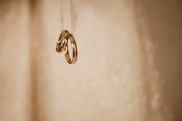 Dos anillos de boda dorados colgados en una cinta, aislados sobre un fondo borroso con reflejos claros — Foto de Stock