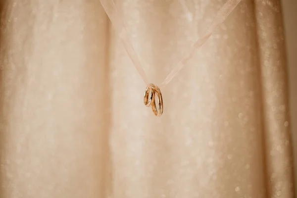 İki altın alyans bir kurdelede asılı, bulanık arkaplanda ışık parıltılarıyla izole edilmiş.