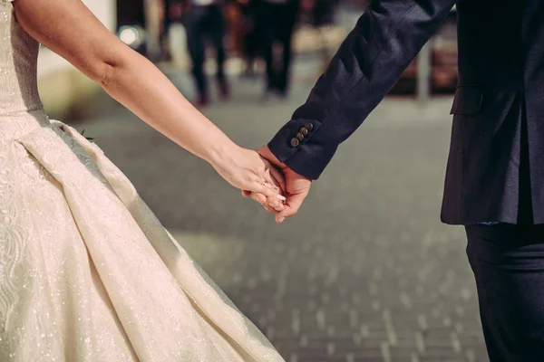 Fecha. Casamento casal está andando de mãos dadas. Em vestido branco e casaco azul — Fotografia de Stock