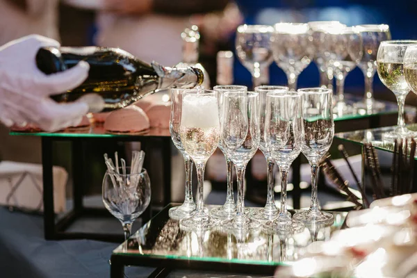 Şampanya dolduran beyaz eldivenli bir el. Beyaz eldivenli garson masaya ayna yüzeyi olan şampanya bardaklarını döktü.