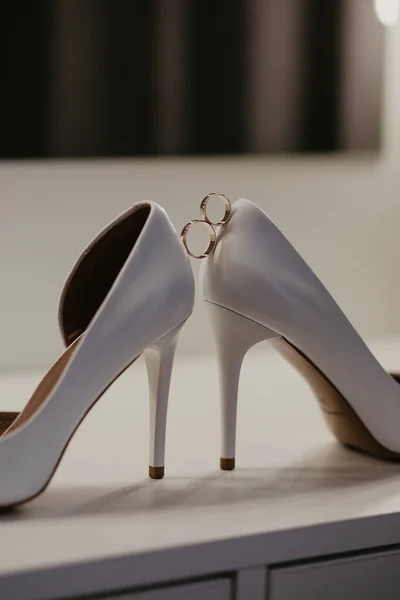 2ホワイトハイヒールの靴のペアの間に2つのゴールドの結婚指輪。鏡の近くのテーブルの結婚式の詳細 — ストック写真