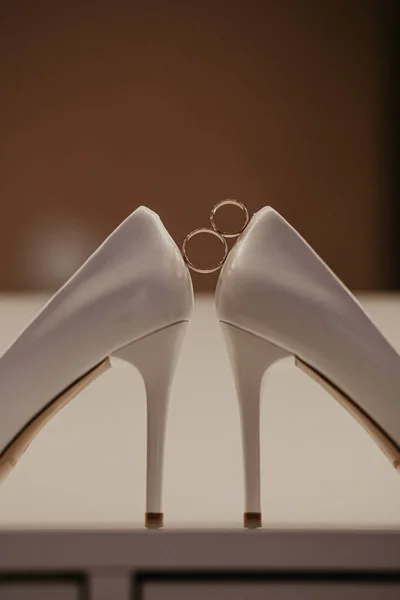 Золотые обручальные кольца между двумя туфлями на высоком каблуке. Свадебные детали на столе возле зеркала — стоковое фото