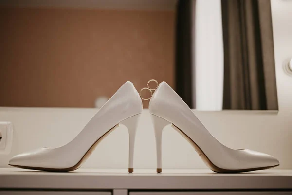 2 Два золотых обручальных кольца между парой туфель на высоком каблуке. Свадебные детали на столе возле зеркала — стоковое фото