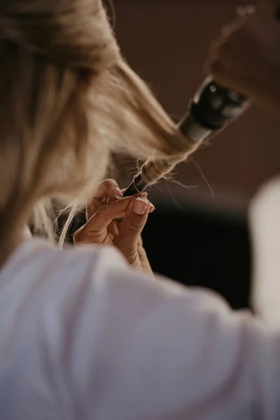 La novia retuerce el cabello con una rizadora en casa. Preparación de la novia. De cerca. Las mujeres que hacen el peinado a sí misma y el uso de plancha en el pelo rizado largo hermoso. Concepto de belleza y cuidado del cabello — Foto de Stock