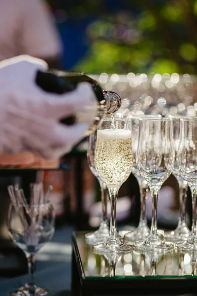 Mâna cu mănuşă albă turnând şampanie. Chelnerul în mănuși albe a turnat pahare de șampanie pe masă cu suprafața oglinzii — Fotografie, imagine de stoc
