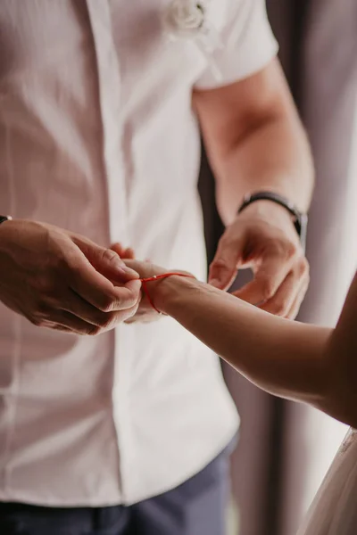 El hombre ata una pulsera roja en la mano de la mujer, hilo rojo, joyas, pulsera con una piedra, accesorios para mujer. Amor auténtico. —  Fotos de Stock