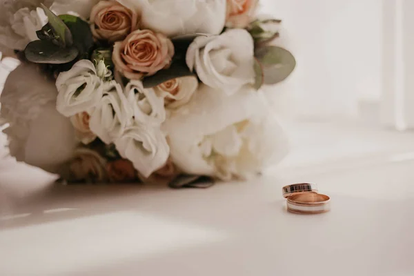 Ramo de bodas con hermosas rosas y piones con 2 anillos de boda tirados en el suelo cerca de la ventana con cortinas. Larga sombra de la ventana — Foto de Stock