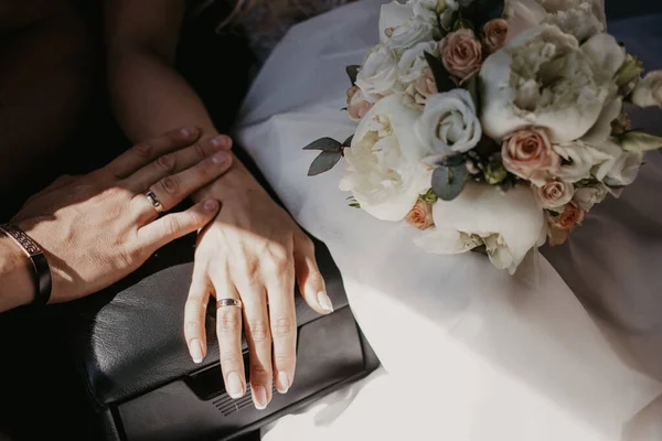 Egy kéz az esküvői pár megérintik egymást. Friss házasok, jegygyűrűvel a kezükben. Menyasszonyi kéz gyűrűkkel a fekete bőr karfán a gyereküléseken. Árnyék a nap miatt — Stock Fotó
