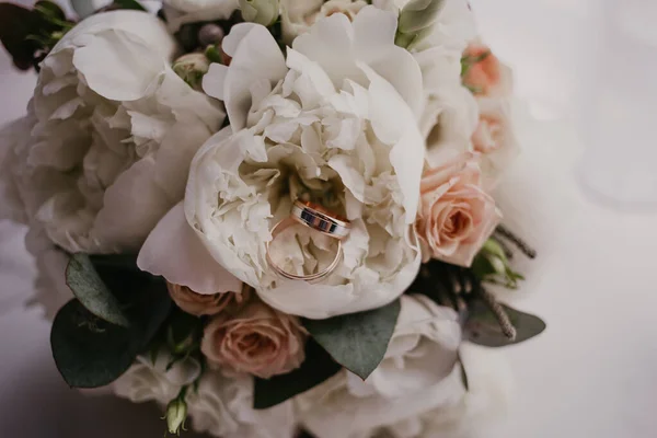 2 anillos de oro en el ramo de bodas con hermosas rosas y piones. Día de la boda. Preparación de boda — Foto de Stock