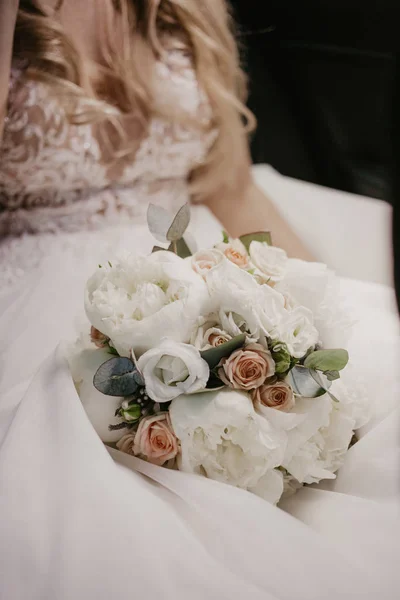 Wedding bouquet in hands of bride. Beautiful bride sitting and holding wedding bouquet with beautiful roses and pions. In white dress and nice monicure. Close up — Stock Photo, Image