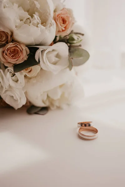 Güzel gülleri olan bir düğün buketi ve perdeleri olan pencerenin yanında duran iki alyanslı bir piyon. Pencerenin uzun gölgesi