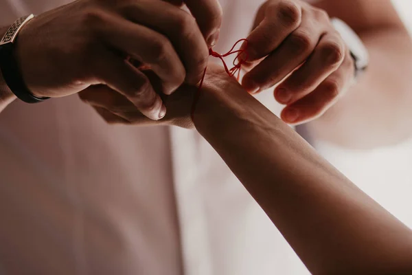 Homem amarra uma pulseira vermelha na mão da mulher, fio vermelho, jóias, pulseira com uma pedra, acessórios femininos. Amor autêntico — Fotos gratuitas