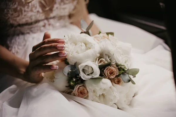 Ramo de boda en manos de la novia. Hermosa novia sentada y tocando el ramo de bodas con hermosas rosas y piones. En vestido blanco y monicura agradable. De cerca. — Foto de Stock