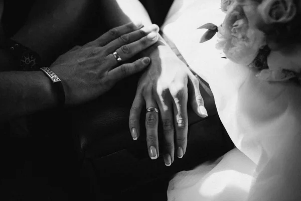 Egy kéz az esküvői pár megérintik egymást. Friss házasok, jegygyűrűvel a kezükben. Menyasszonyi kéz gyűrűkkel a fekete bőr karfán a gyereküléseken. Monokróm. Fekete-fehér — Stock Fotó