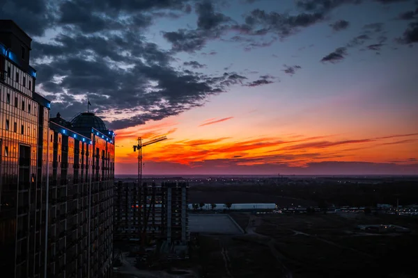 Silhueta de guindaste de construção e construção sobre fundo céu por do sol com nuvens vermelhas e azuis. Silhueta escura de guindaste de construção e construção no céu por do sol. Odesa, Ucrânia. Kadorr... — Fotografia de Stock