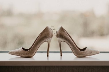 Altın alyanslar bir çift yüksek topuklu ayakkabı arasında. Düğün detayları panoramik pencerenin yanındaki ayna zemininde