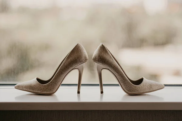Золотые обручальные кольца между парой туфель на высоком каблуке. Детали свадьбы на зеркальном полу рядом с панорамным окном — стоковое фото