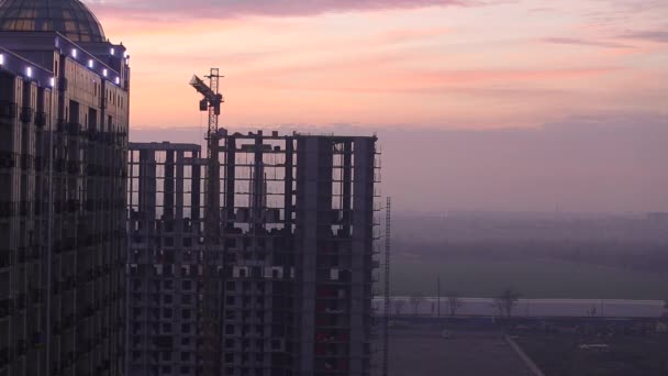 塔式起重机移向侧边 夕阳的天空映衬着未完工的房子 建筑工地高楼正在建设中 房地产 经济学 建筑业背景概念 — 图库视频影像