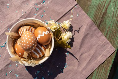 Paskalya bayramı için çeşitli beyaz desenli boyanmış kahverengi yumurtalar. Pamuk mor masa örtüsünde, güneş ışığı ve gölgeli. Dekorasyon mavi şeker ve çiçek, Doğu Avrupa Ortodoks kültürleri