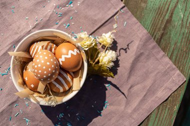 Paskalya bayramı için çeşitli beyaz desenli boyanmış kahverengi yumurtalar. Pamuk mor masa örtüsünde, güneş ışığı ve gölgeli. Dekorasyon mavi şeker ve çiçek, Doğu Avrupa Ortodoks kültürleri