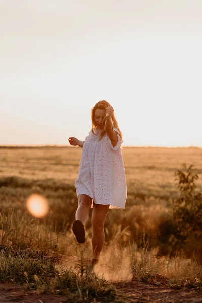 Jovem mulher grávida bonita em vestido branco andando no campo de trigo laranja em um dia ensolarado de verão. Natureza no campo. Esperança de milagres. Pôr do sol no isolamento — Fotografia de Stock