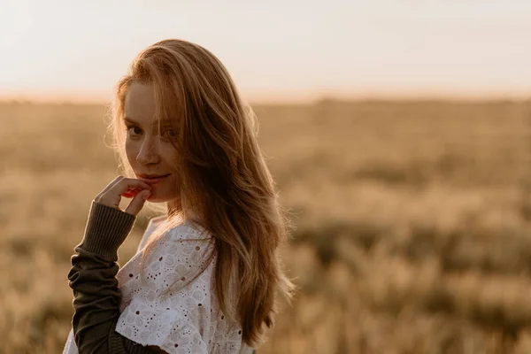 Güneşli bir yaz gününde, turuncu buğday tarlasında yürüyen beyaz elbiseli hamile bir kadın. Ülkedeki doğa. Mucize beklentisi. İzolasyonda gün batımı. Boşluğu kopyala