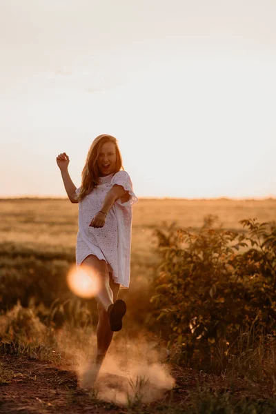 Jovem mulher bonita fazendo poeira com o pé e gritando no campo de trigo laranja em um dia ensolarado de verão. A enlouquecer. Sentindo-se livre e feliz. Esperança de milagres. Pôr do sol no isolamento. Brilho solar — Fotografia de Stock