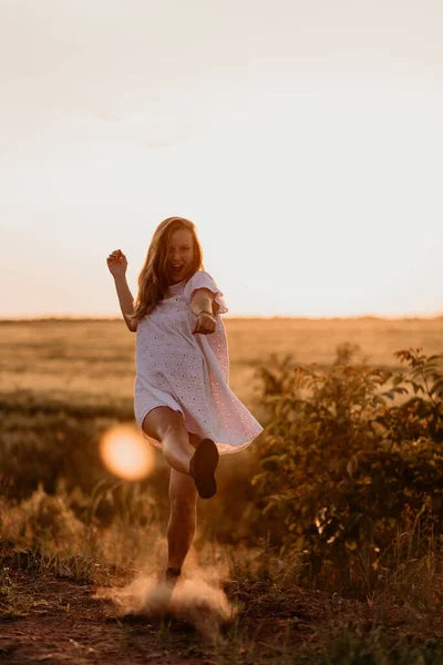 Jovem mulher bonita fazendo poeira com o pé e gritando no campo de trigo laranja em um dia ensolarado de verão. A enlouquecer. Sentindo-se livre e feliz. Esperança de milagres. Pôr do sol no isolamento. Brilho solar — Fotografia de Stock
