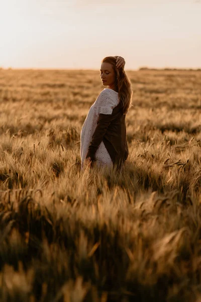 Young beautiful pregnant woman in white dress walking in the wheat orange field on a sunny summer day. Nature in the country. Miracle expectation. Sunset on isolation — Stock Photo, Image