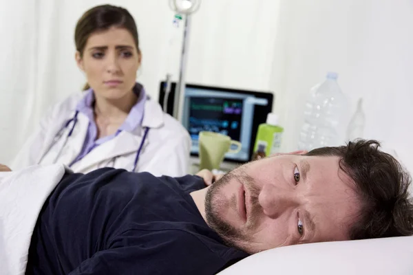 Verzweifelter kranker Mann im Krankenhausbett, der fast vor Heilung weint. Arzt sitzt neben ihm — Stockfoto