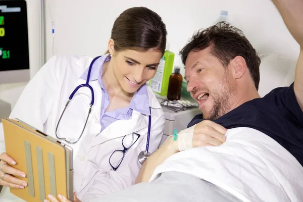 Χαρούμενος ο γιατρός δείχνει καλό διαγνωστικά αποτελέσματα δοκιμών σε έναν ασθενή που βρίσκεται στο κρεβάτι του νοσοκομείου. — Φωτογραφία Αρχείου