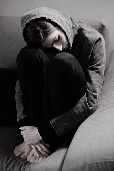 Jonge vrouw triest en depressief op bank holding knieën — Stockfoto
