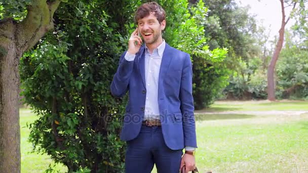 Feliz hombre de negocios caminando y hablando por teléfono en el parque de tiro medio — Vídeos de Stock