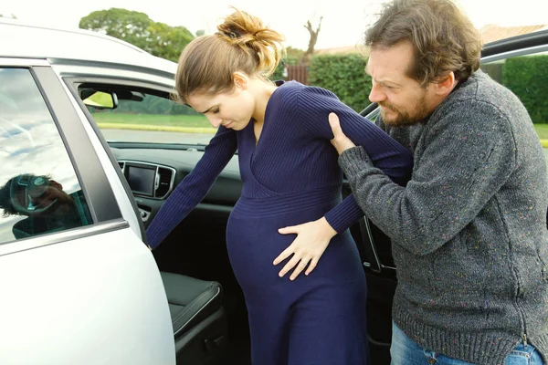 Mujer embarazada sintiendo dolor ayudó a entrar en el coche por novio — Foto de Stock