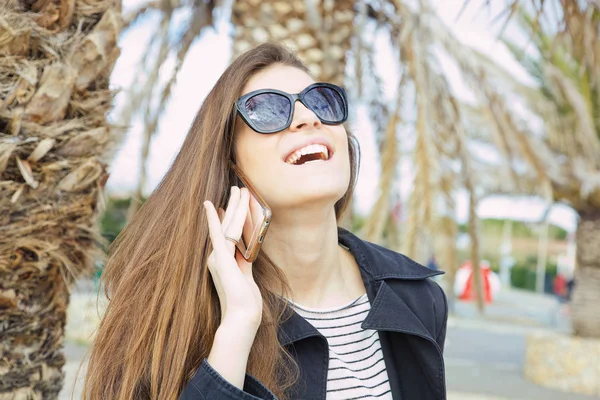 Hermosa mujer riendo en gafas de sol hablando en el teléfono móvil fuera en vacaciones Imágenes De Stock Sin Royalties Gratis