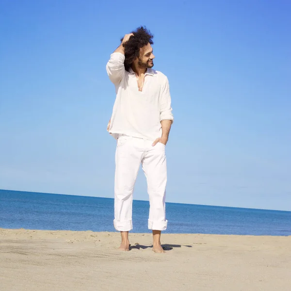 Cool man smiling standing on sand in front of the ocean touching afro hair — Stock Photo, Image