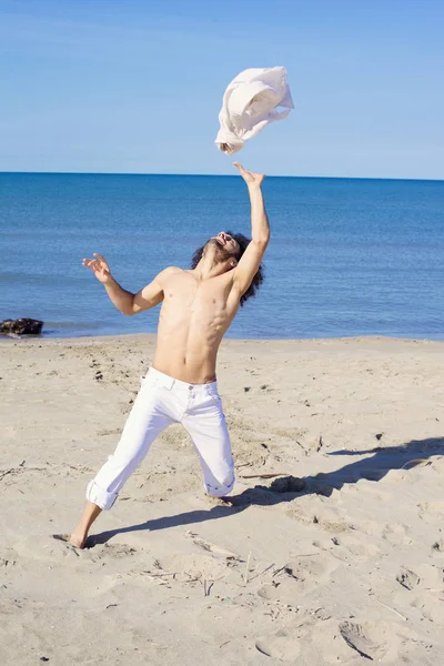 Hombre fresco lanzando camisa en el aire frente al océano Imágenes de stock libres de derechos