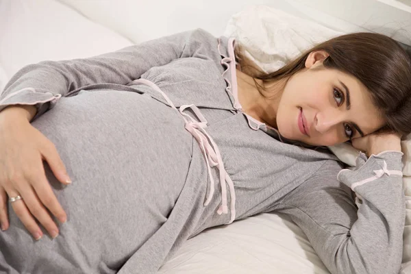 Cute young pregnant woman smiling looking camera lying in bed — Stock Photo, Image