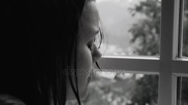 Woman with wet hair in front of window with rain feeling lonely closeup black and white — Stock Video