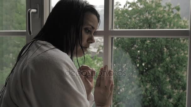 Женщина с мокрыми волосами перед окном с дождём — стоковое видео