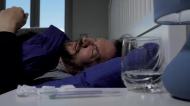 Çok şiddetli baş ağrısı ve ateşi olan hasta bir adam yatakta.