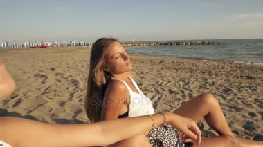 Dolly iki kız güneşlenme mutlu gün batımında sahilde orta Shot closeup vurdu