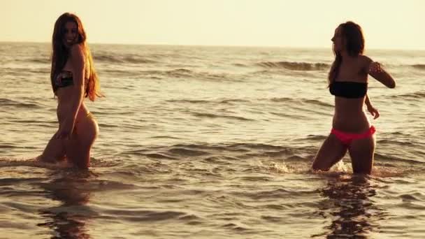 Niedliche junge Frauen tanzen im Sommer im Wasser des Ozeans bei Sonnenuntergang in Zeitlupe — Stockvideo