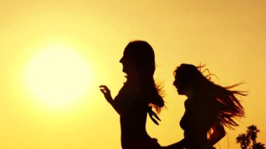 Bikini önünde güneş batımında sahilde çalışan iki genç kadın silüeti