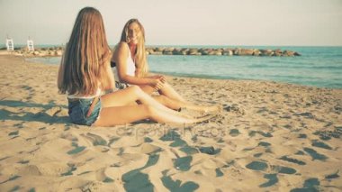 Ağır çekim retro analog tarzı gülümseyen sahilde oturup uzun saçlı güzel sarışın kız