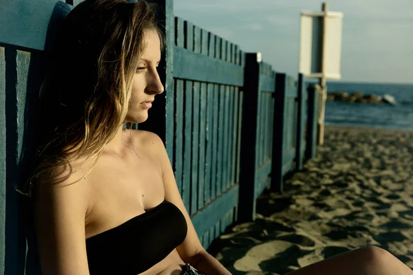 孤独忧郁的年轻金发女子沉思在日落时分坐在海滩上 — 图库照片