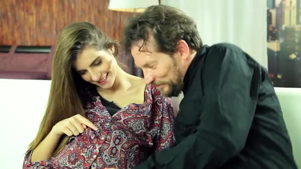Glücklich schwangere Frau sitzt auf Sofa Ehemann spricht mit Bauch — Stockvideo
