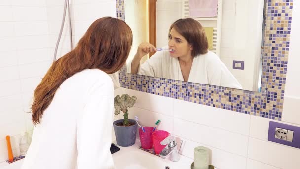 Linda mujer feliz riendo mientras se lava los dientes delante del espejo de tiro ancho — Vídeos de Stock