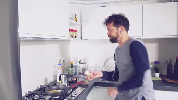 Человек готовит яйца, посыпая соль на кухню во время танцев — стоковое видео